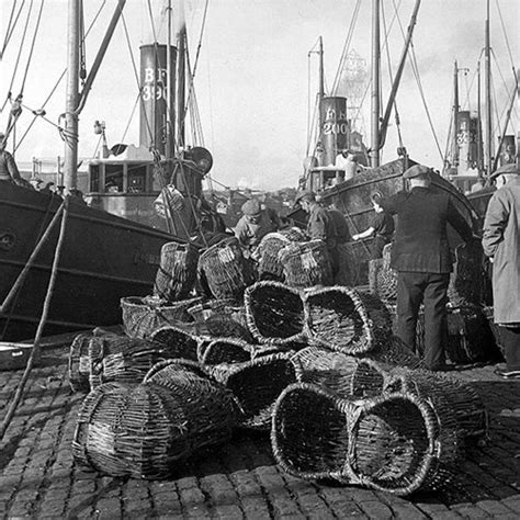 Swill fishing baskets on the quay at Great Yarmouth, herring steamers (boats) in the background.